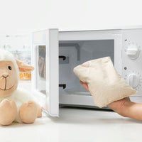 Sheep Soft Toy with Warming and Cooling Effect Wooly InnovaGoods next to a microwave for warming.